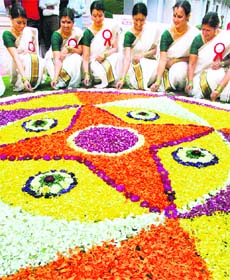 Women pose in front of a traditional flower arrangement called "Pookalam" during Onam celebrations in Hyderabad