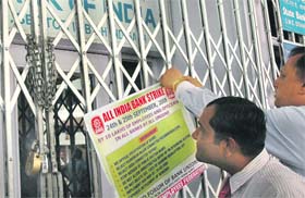 A man looks at a poster being put on the locked gates of a bank in Sector 7, Chandigarh, informing customers of the 2-day bank strike