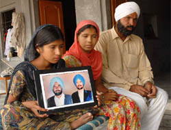 Daughters of Ranjeet Singh show the photographs of their father and their brother, who died of cancer, at Bhaliana village in Muktsar district.