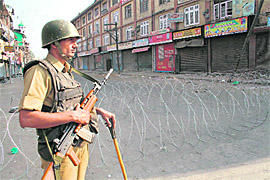 A CRPF soldier stands guard near a barbed wire barricade in Srinagar on Sunday. Indefinite curfew was imposed in all 10 districts of the valley to prevent people from reaching Lal Chowk. 