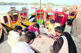 Idle Kashmiri shikara owners while away time playing carrom on the banks of Dal Lake on Tuesday.