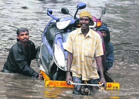 Rickshaw-pullers transport motor cycles down a flooded road after a heavy rain in Chennai