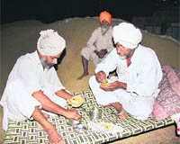 Farmers have dinner by heaps of paddy at a mandi in Bathinda on Tuesday.