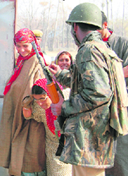 A jawan stands guard as Kashmiri women await their turn to cast vote outside a polling station at Langate, 85 km from Srinagar, on Sunday.