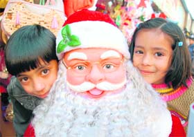 Two kids smile by posing with Santa Claus dummy at The Mall in Shimla
