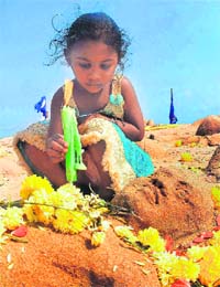 A girl lights a candle near a sand replica of a body, signifying tsunami, on the occasion of the fourth anniversary of the killer waves in Chennai