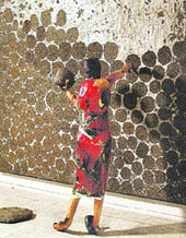 A three-dimensional collage by Shakila which shows a village woman putting cowdung cakes on the wall of a mud house 