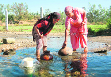 Women fill water in their earthen utensils from a natural source.