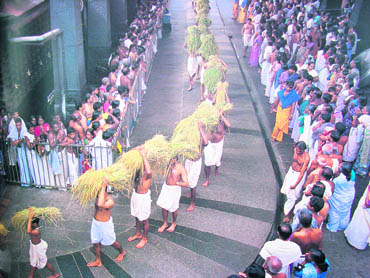 Temple functionaries carry loads of paddy sheaves brought in as offerings at Guruvayur temple, Kerala Photograph by Pepita Seth