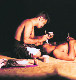 A chuttikkar applies the rice flour and limestone paste on a performers face. Preparing the make-up and fixing the frame around the face needs precision