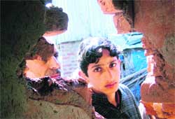 A boy and a man look through the damaged wall of a house where a Lashkar-e-Taiba militant, Abu Hamza, was killed in an encounter with security forces at Amargarh village in Sopore