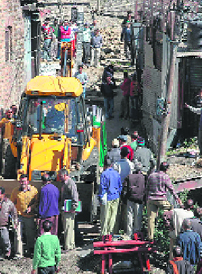 Northern Railway officials clearing land with the help of a JCB machine encroached upon by residents, in Shimla on Thursday.
