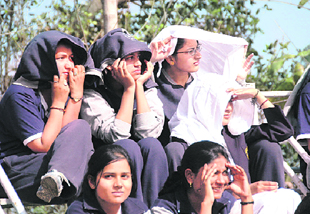 Girls protect themselves from sun while watching a match in Dehradun.