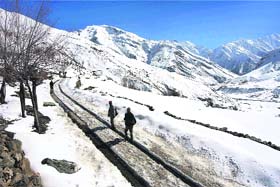 People walk on a snow-covered road after snowfall in Tholang village in Keylong