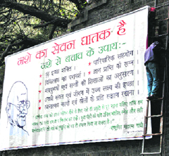 A hoarding highlighting government achievements being covered by a banner with a social message to comply with the code of conduct.