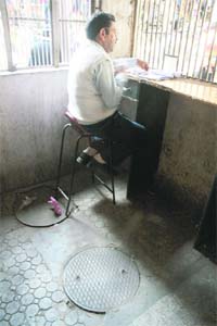 A ticket booking employee sits in a cabin with a manhole in the center in the premises of main bus stand in Jammu