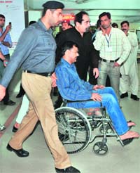 A Pakistani policeman escorts arrested former Pakistan batsman Ijaz Ahmed (C) in a wheelchair at a hospital in Lahore