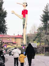 People walking towards a 16-metre-tall statue of fictional fib-prone puppet, Pinocchio, a Guinness world-record holding creation, are seen from a street at Collodi village in Italy