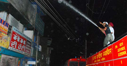 Fire brigade personnel dousing the flames that gutted a shop in the supermarket near the bus stand in Bathinda