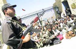 A Pakistani border police officer stands guard as Afghan prisoners who are released by Pakistani authorities wait to enter neighboring Afghanistan at Pakistani border post in Chaman on Friday