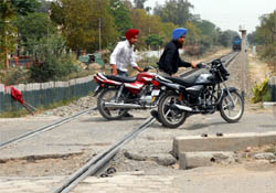 Two bikers (left) cross even as a railway engine moves towards a manned railway crossing in Bathinda on Saturday