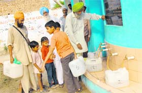 Children and their parents fill cans of filtered water from an RO plant at Bhaliana village in Muktsar district