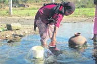 A woman fills up earthen pots with water from a natural sourcet