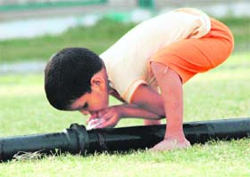 A child quenches his thirst from a leaking water pipe in a park in Gurgaon