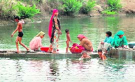 Village women wash clothes while children take a splash in a pond to beat the summer heat in the water-starved Mewat area