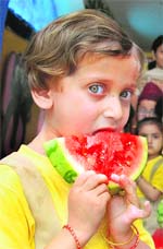 A little girl enjoys a watermelon slice on a hot and sultry day during the Watermelon Day celebrations in a school in Jammu
