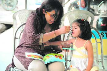 A woman feed her little one as she reads a book in Dehradun 
