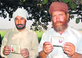 Two farmers of Roranwala Khurd village situated on the Indo-Pak border show their identity cards for crossing the barbed fence for cultivation