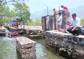 A man fishes in a canal while children enjoy the cool water in Dehradun on Wednesday. 