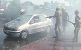 Fire fighters splash water on a car that suddenly caught fire at Cannought Place in New Delhi on Thursday.