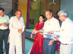 Mohinder Kumar, commissioner, Ambala division, distributes cheques among beneficiaries at a sammelan of sarpanches in Kaithal.
