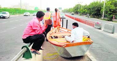 Workers wait for a vehicle to ferry them and their boat to a suitable place from this busy Gurgaon road