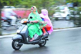 A woman and her children take help of her duppatta and a plastic sheet, respectively, to seek protection from rain in Jalandhar