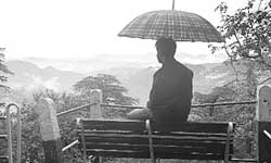 A man sitting near the vidhan sabha building in rain, obviously enjoying weather, at Shimla 