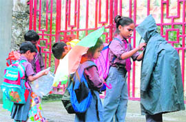 A girl helps her schoolmate wear a raincoat at Rajpur road in Dehradun on Wednesday.