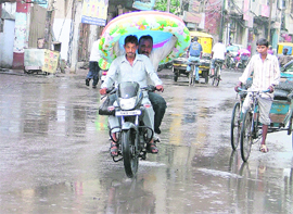 A man riding pillion on a motorcycle use baby’s pool to protect themselves from the rains .