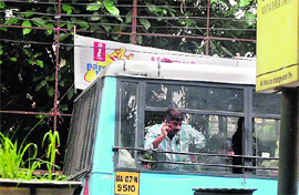 A man hangs out of a moving bus to ensure better signal on his cell phone in Dehradun on Friday.