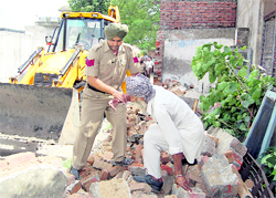 A policeman tries to remove a senior citizen, who sat in front of the JCB machine, protesting against the demolition drive in Ludhiana on Saturday.