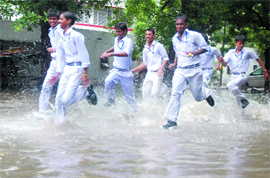 Schoolboys run on a waterlogged road after rain near Bal Bhavan at ITO in New Delhi on Saturday. 