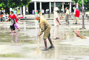 Workers sweep rainwater off the paved area at Sector 17 plaza following rain in Chandigarh on Wednesday. 