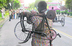 A knife-sharpener carries his machine at Rajpur Road in Dehradun on Friday.