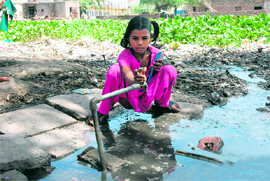 A child turns on a tap to drink water in filthy conditions at Budhanpur village of Panchkula.
