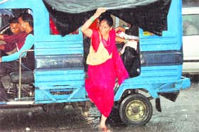 A woman shelters herself from rain while getting down an auto in Dehradun