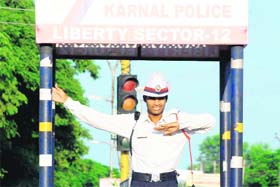 A policeman, sporting a white hat in place of the conventional helmet, mans traffic at Nirmal Kutia Chowk on the NH-1 in Karnal