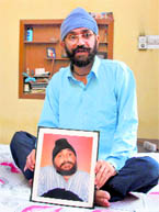 A riot victim, Tejinder Singh, holds the picture of his brother, Gurcharan Singh, who had remained bedridden for 25 years before dying earlier this year.