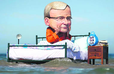 A man wearing a mask depicting Australias Prime Minister Kevin Rudd sits on a bed at a beach in Melbourne as part of a global climate wake-up call orgainsed by Oxfam Australia on Monday.